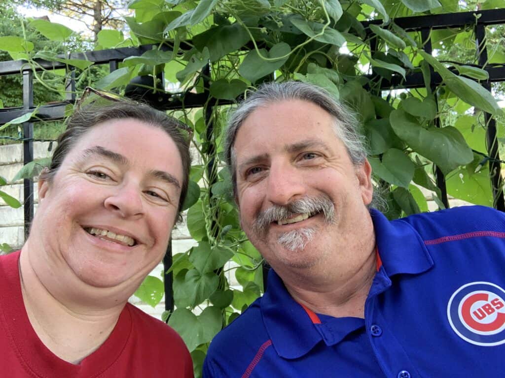 Green climbing plants on trellis with two smiling people in front.