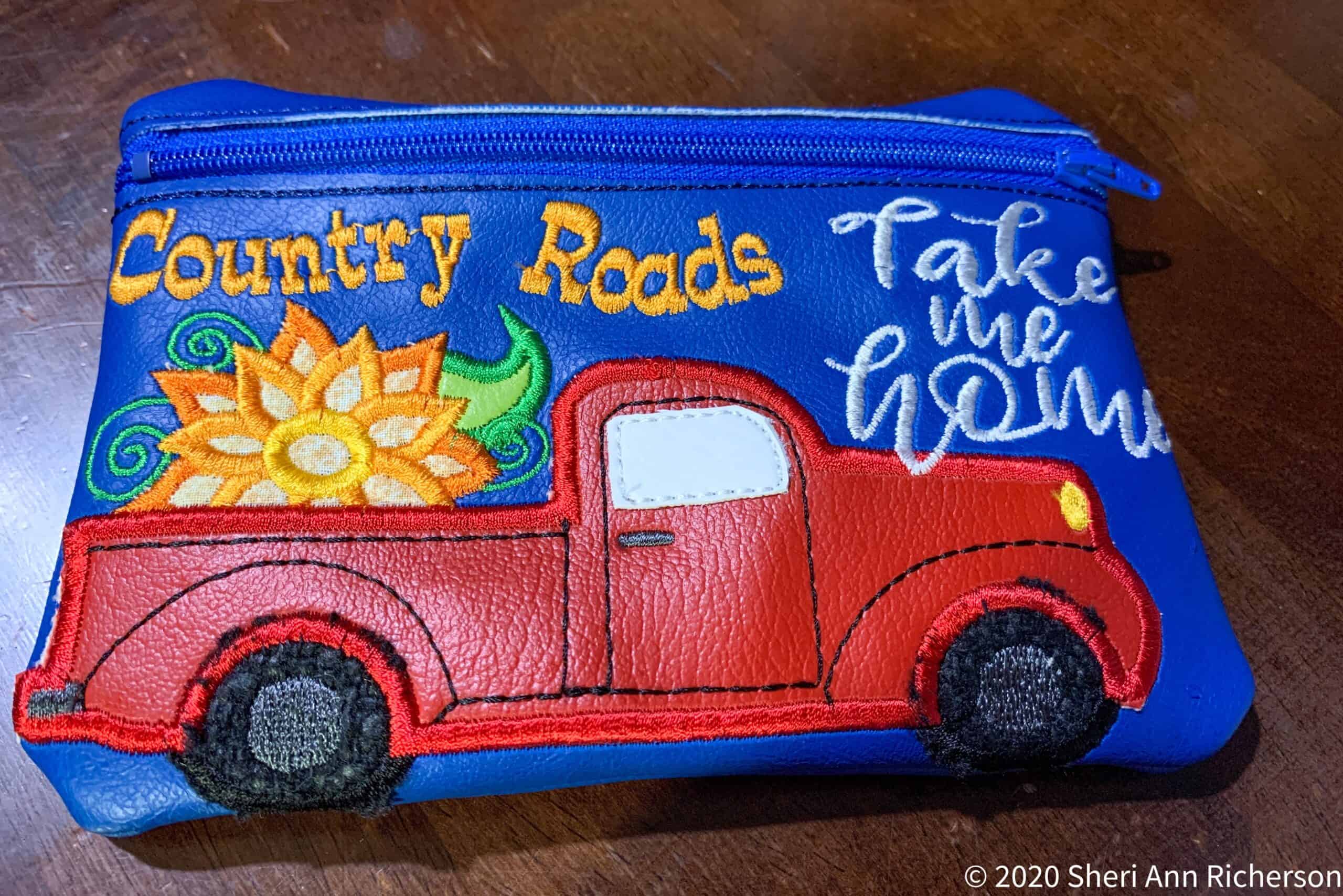 Colorful embroidered pouch featuring a red truck and floral design with "Country Roads" and "Take me home" text.