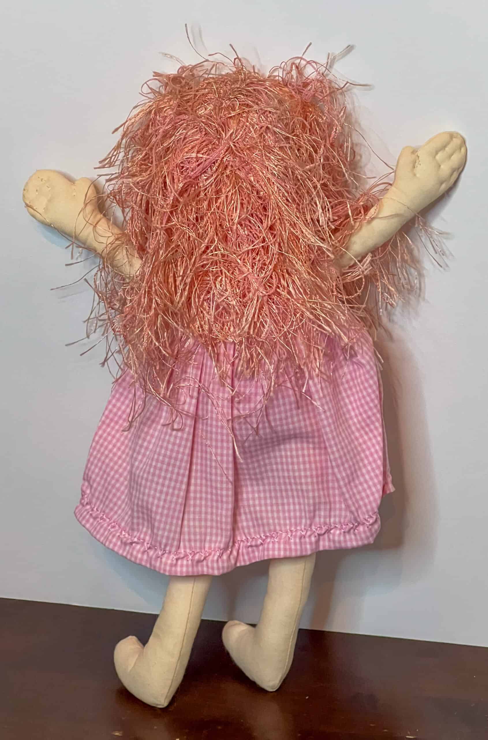 Fluffy pink troll doll with yarn hair and gingham dress.