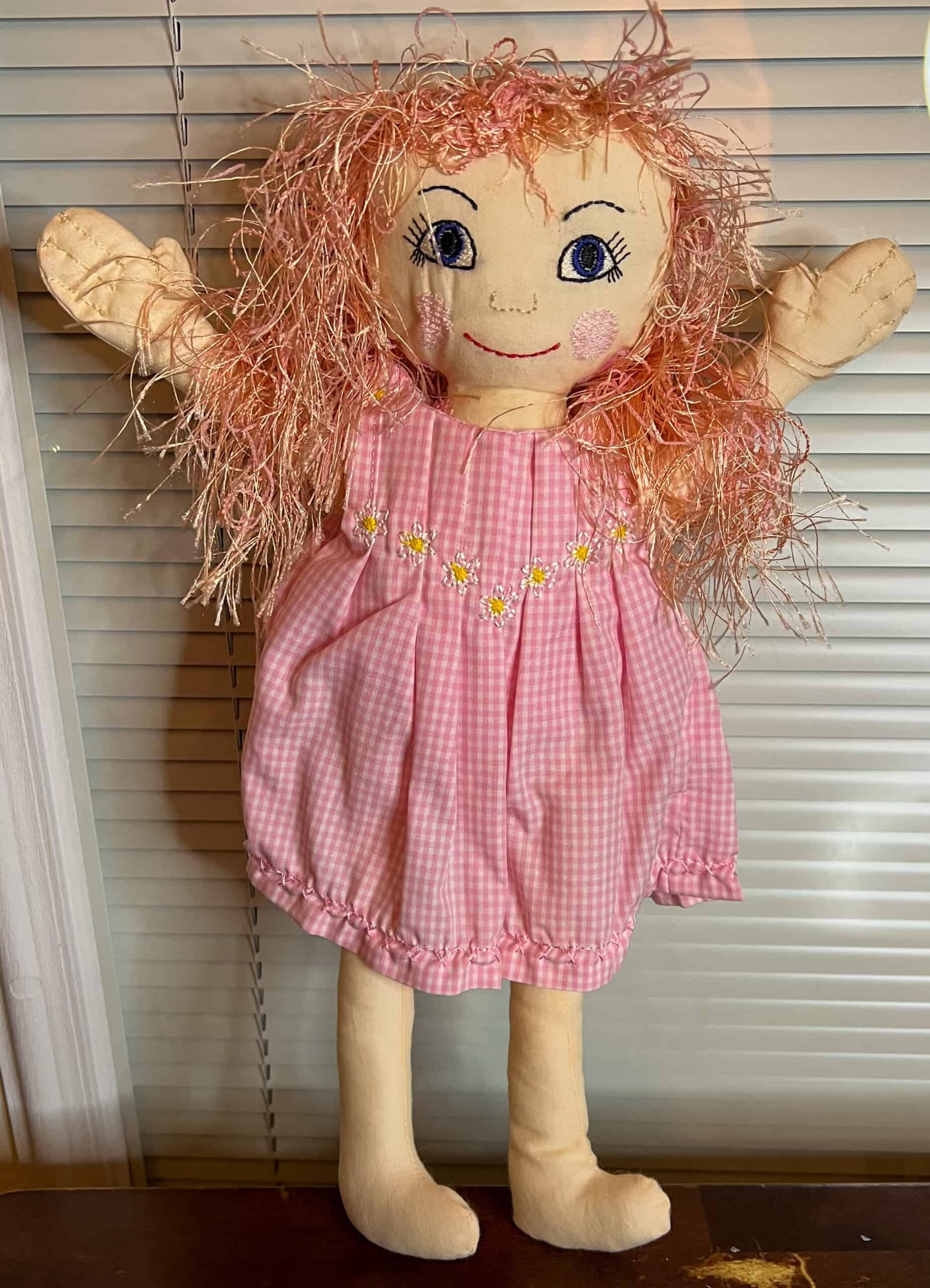 Pink scarecrow doll with embroidered dress and yarn hair, perfect for homesteading decor.