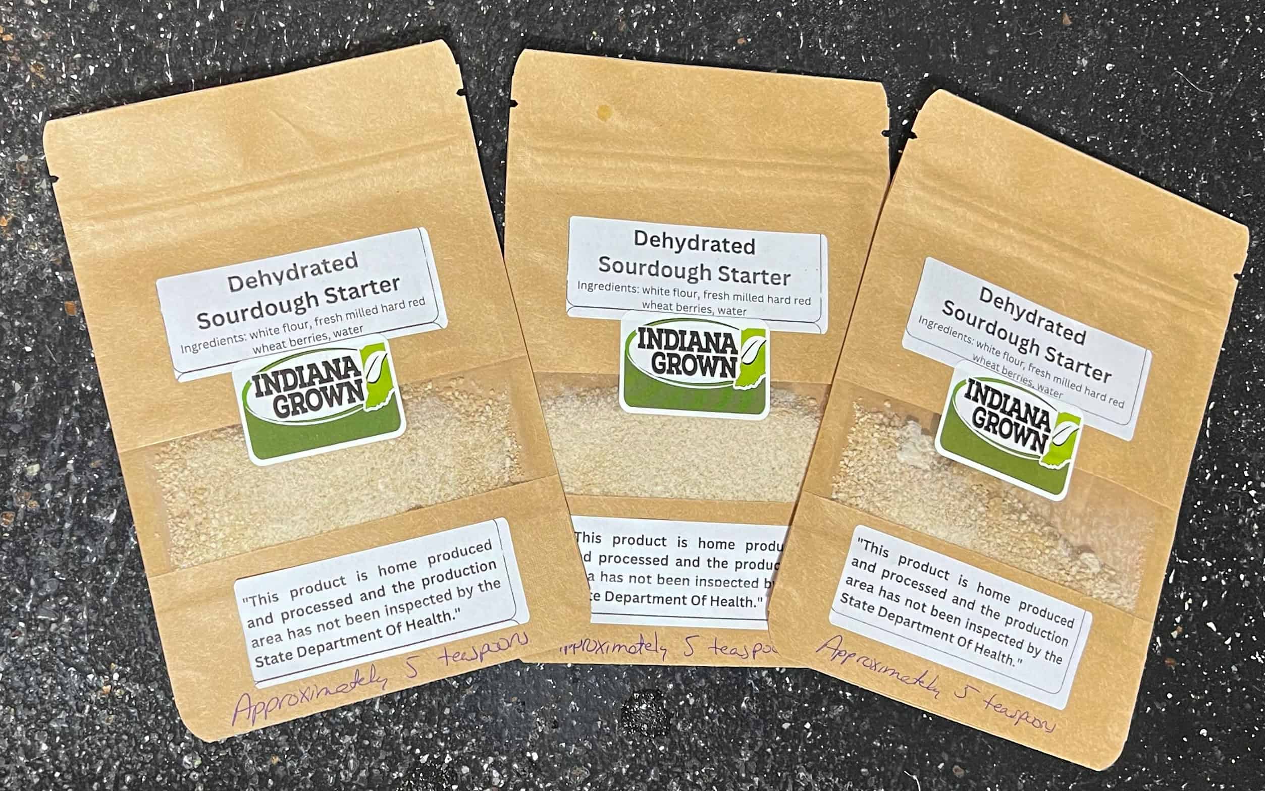 Dehydrated sourdough starter packets on a black surface with handwritten label reading "Approximately 5 teaspoons.".
