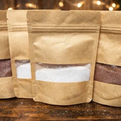 Three kraft paper gourmet hot cocoa single-serving pouches photographed together on a wooden table